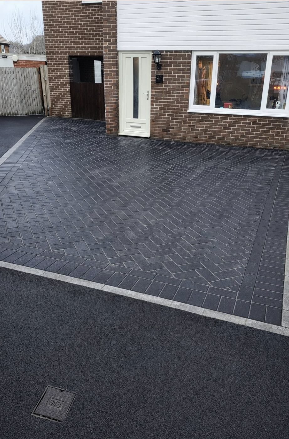 Charcoal block paved driveway laid in herringbone with a light soldier course border, running up to a house door