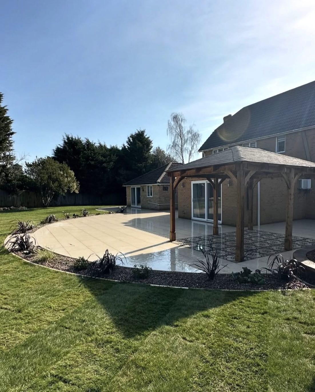 Curved cream porcelain patio sweeping around a house with a timber gazebo and gravel planting margin