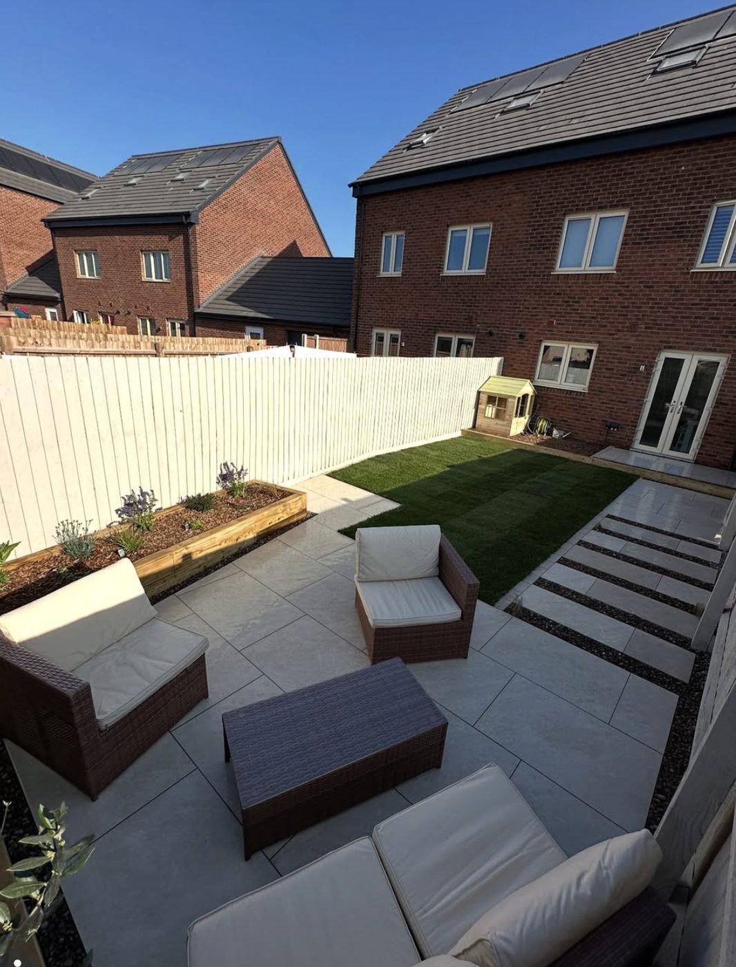 Grey porcelain patio with rattan seating, a sleeper raised bed and porcelain stepping stones set through the lawn