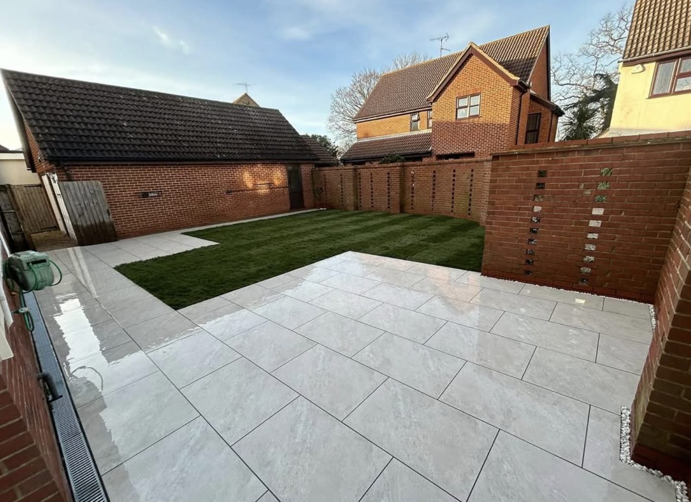 Light porcelain patio with a freshly laid turf lawn behind it, enclosed by brick walls