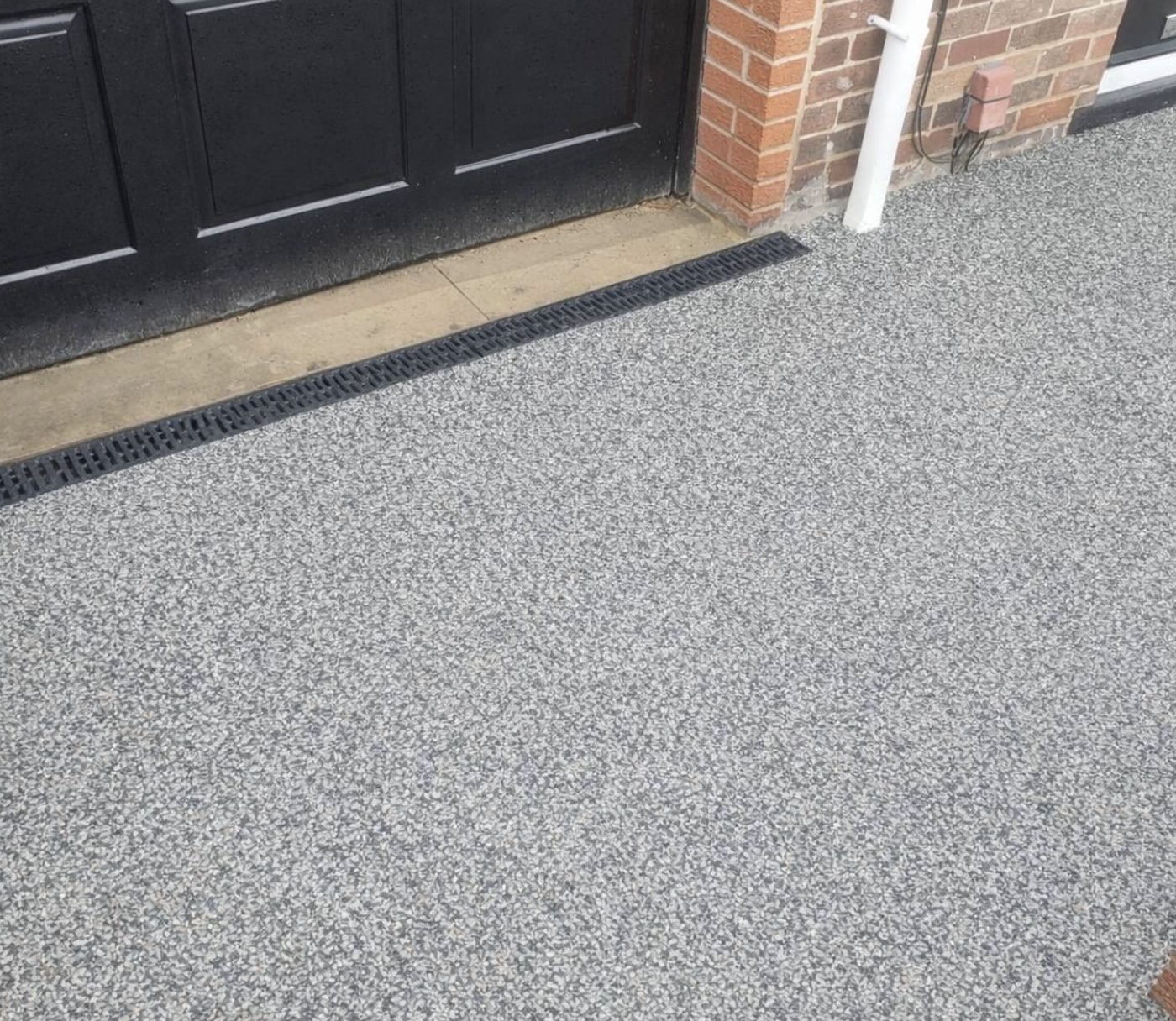 Close view of a resin bound driveway meeting a channel drain and threshold at a black front door