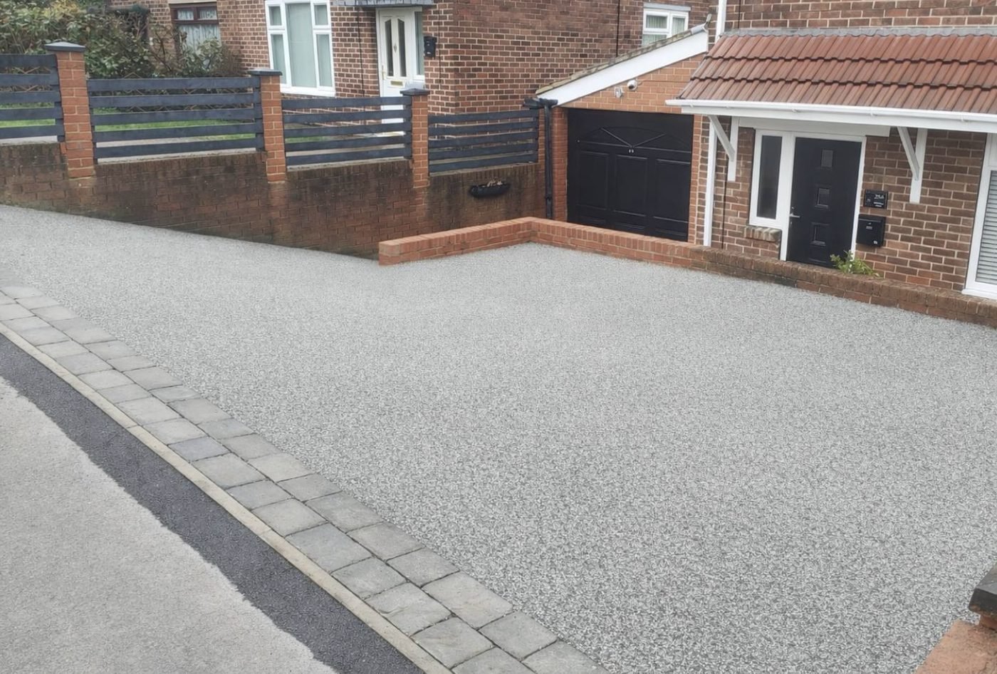 Light grey resin bound driveway with a stone sett border running down to the road