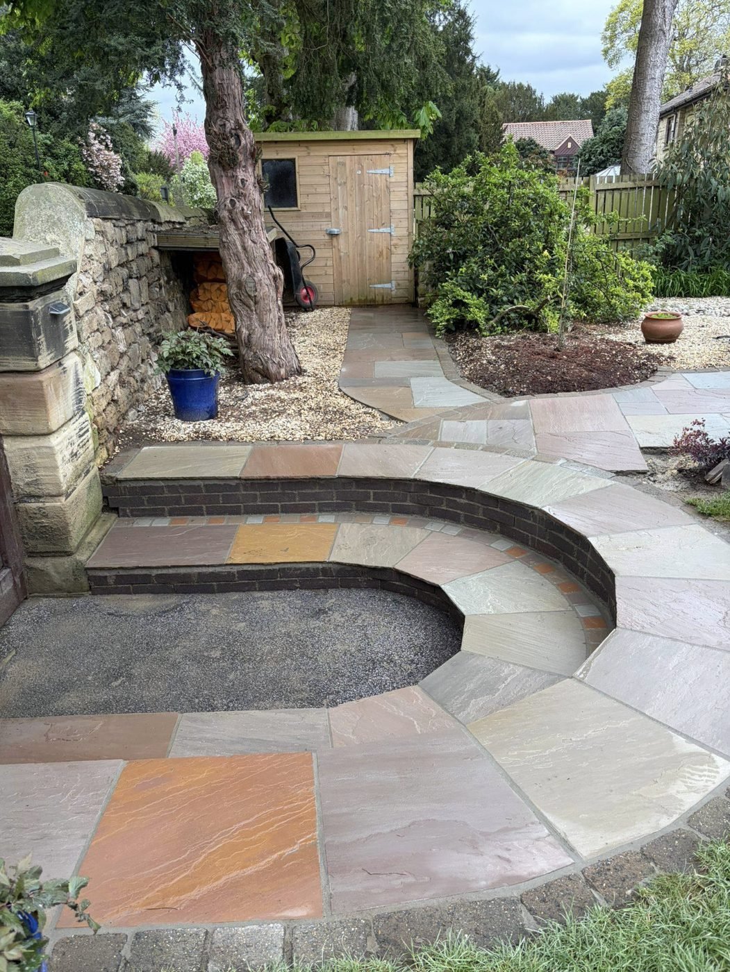 Curved Indian sandstone patio with brick-edged radius steps sweeping round to a shed and gravel bed