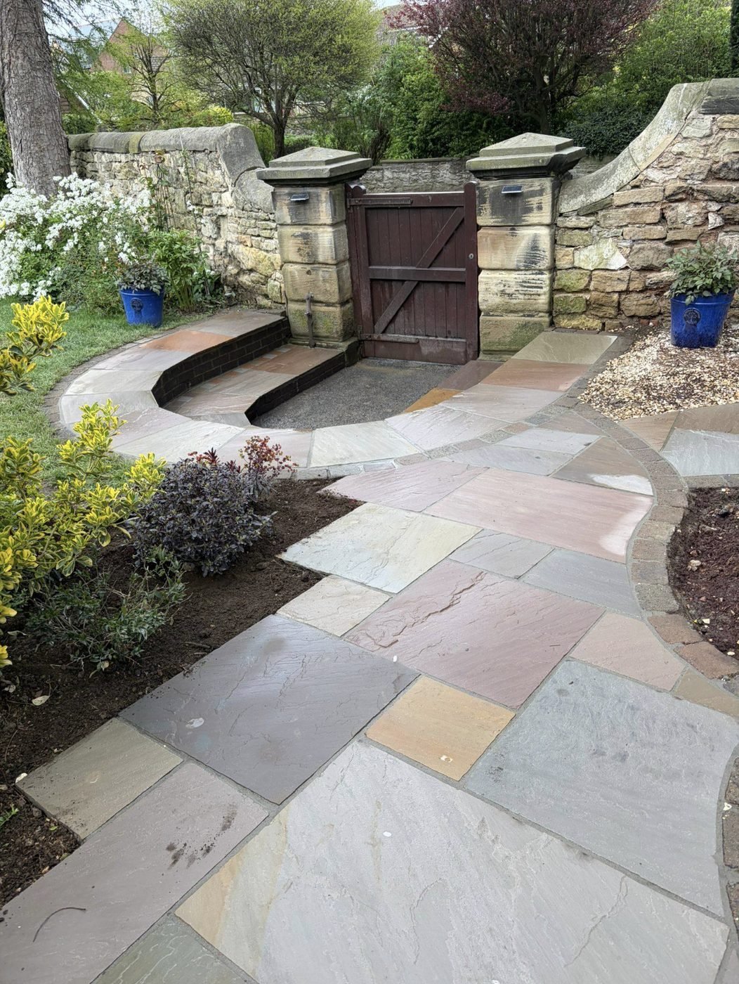 Indian sandstone path curving through a stone-walled garden to a timber gate between stone gate posts